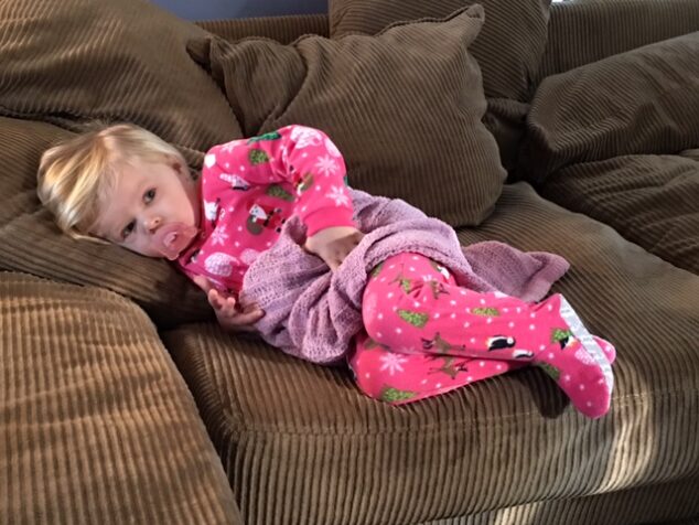 little girl in carters christmas pajamas on brown couch